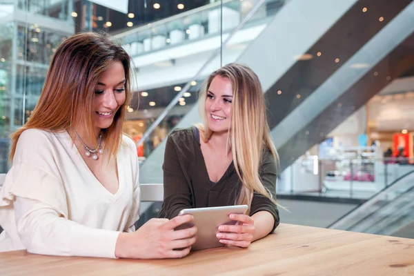 Dos chicas usando tableta digital viendo contenido multimedia en un café en un centro comercial —  Fotos de Stock