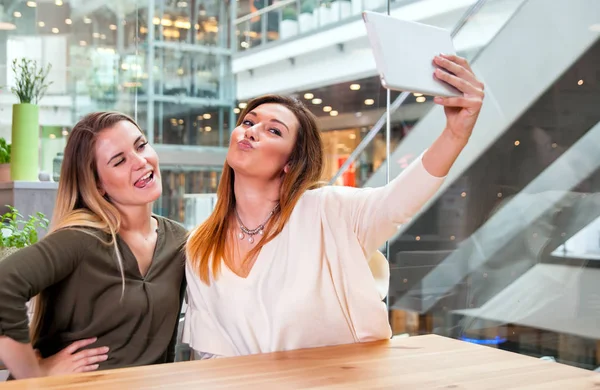 Две девушки делают селфи с цифровым планшетом в кафе в торговом центре — стоковое фото