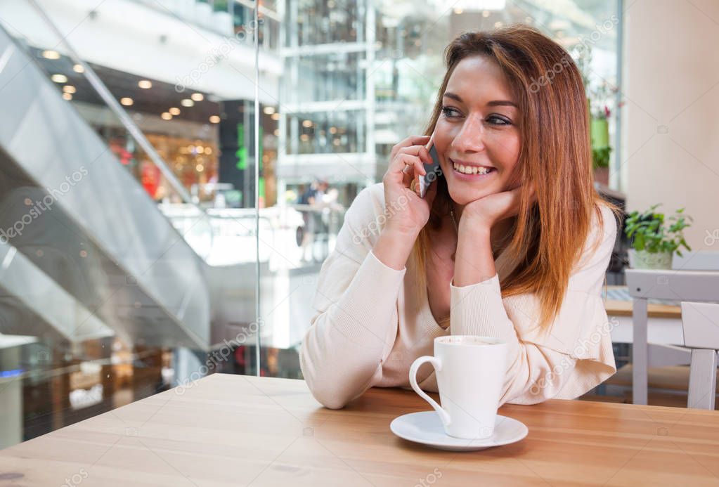 Girl talking on mobile phone in cafe at shopping mall