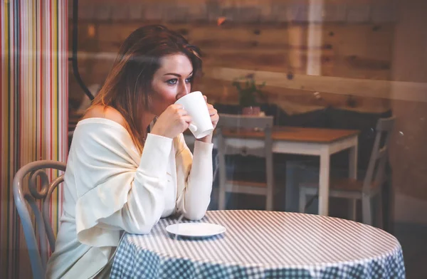 Ensam kvinna som tittar på något i café under dricka kaffe — Stockfoto