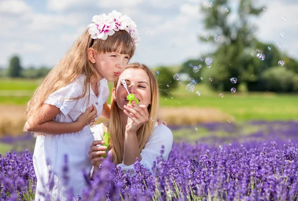Мать и дочь надувают мыльные пузыри в лавандовом поле счастливыми — стоковое фото