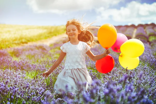 Linda niña corre con globos de colores en el campo de lavanda concepto de libertad de verano —  Fotos de Stock