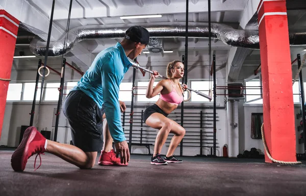 Fit femme faisant des exercices de squats d'haltères avec l'aide d'un entraîneur à la salle de gym — Photo