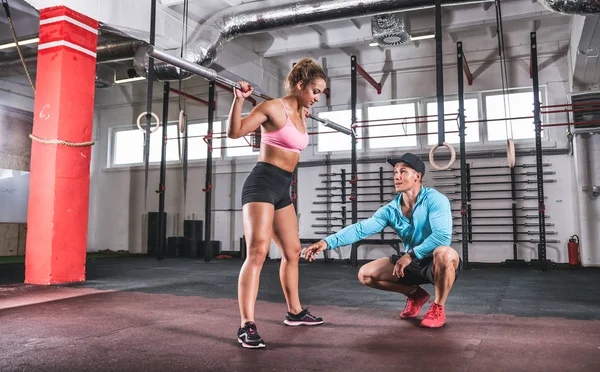Fit vrouw doen halter kraakactie oefening met hulp van trainer bij gym — Stockfoto