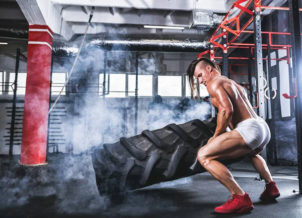 Bodybuilder athlétique musculaire pneu flipping dans la salle de gym cross — Photo