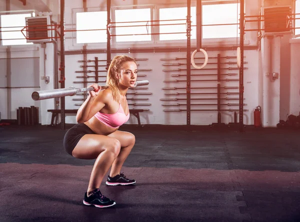 Gespierde vrouw doen squats met barbell op sportschool — Stockfoto