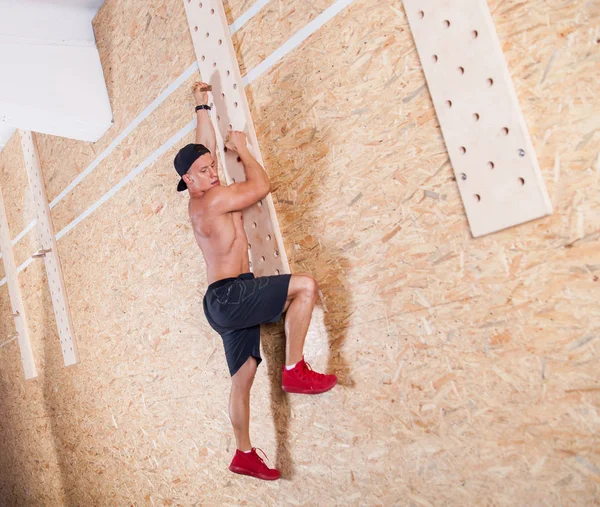 Muscular man climbing peg board in gym
