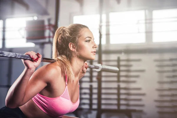 Muscular girl doing squats with barbell at gym, close up portrait