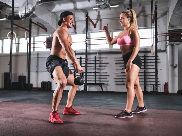 Homem muscular fazendo kettlebell exercer com a ajuda do treinador no ginásio — Fotografia de Stock