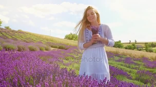 junge Frau mit Bouquet von frischem Lavendel geht in Lavendelfeld