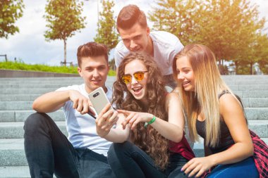 Grup oturan arkadaşıyla birlikte telefon kullanarak ve gülüyor