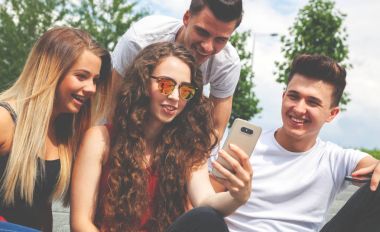 Grup oturan arkadaşıyla birlikte telefon kullanarak ve gülüyor