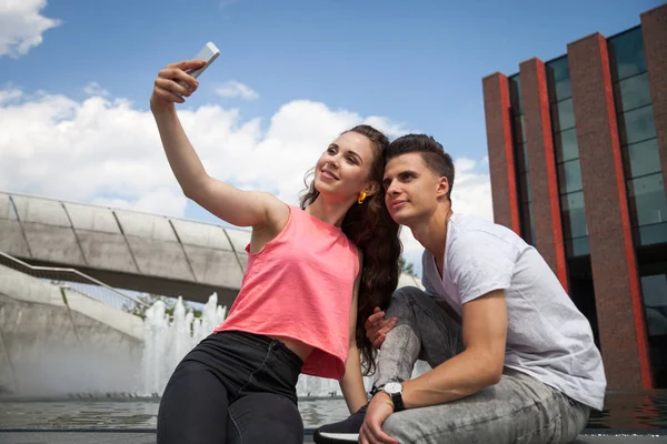 Młoda para siedzi w mieście odkryty z telefonu komórkowego biorąc selfie — Zdjęcie stockowe
