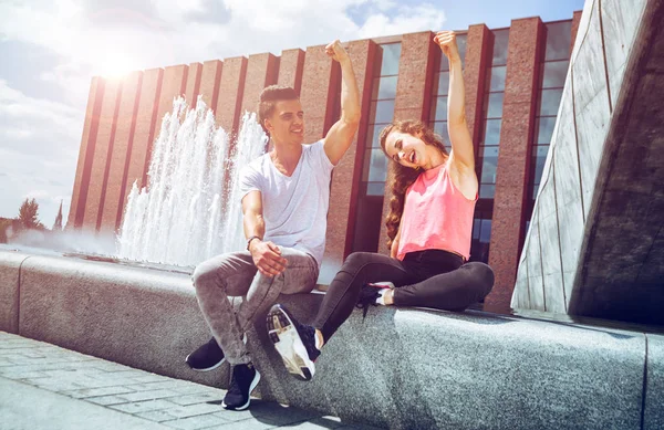 Joven pareja sentado al aire libre y mostrando fuerte brazo, éxito con —  Fotos de Stock