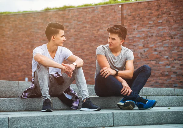 Two friends casual wear sitting on stairs in town and talking, b