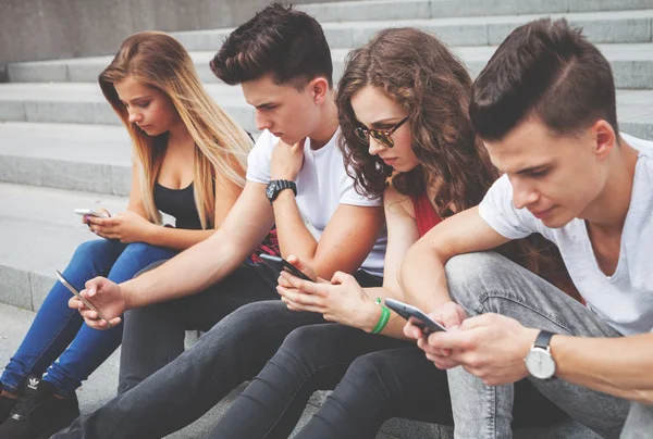 Groupe d'amis assis ensemble en utilisant leurs téléphones — Photo