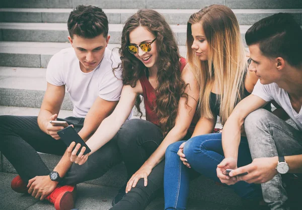 Groep vrienden zitten samen met behulp van telefoon- en lachen — Stockfoto