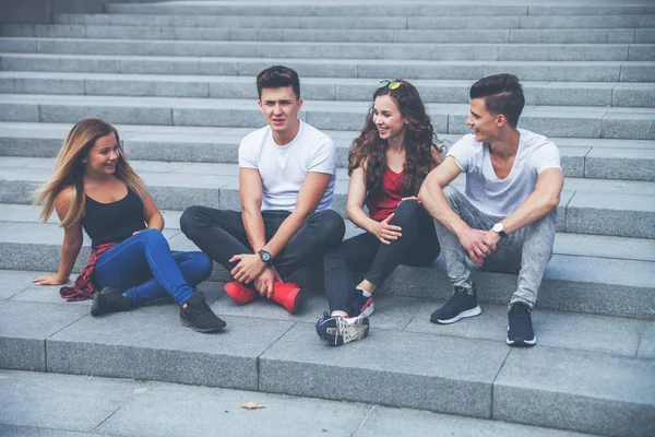 Group of friends sitting together on stairs and talking, city background — Stock Photo, Image