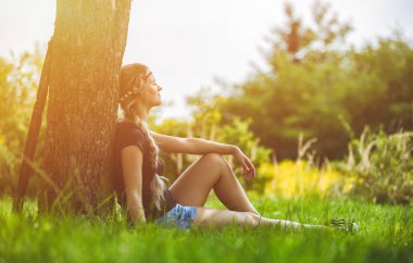 Ağacın altında oturan çayır üzerinde yaz gününde hippi kız