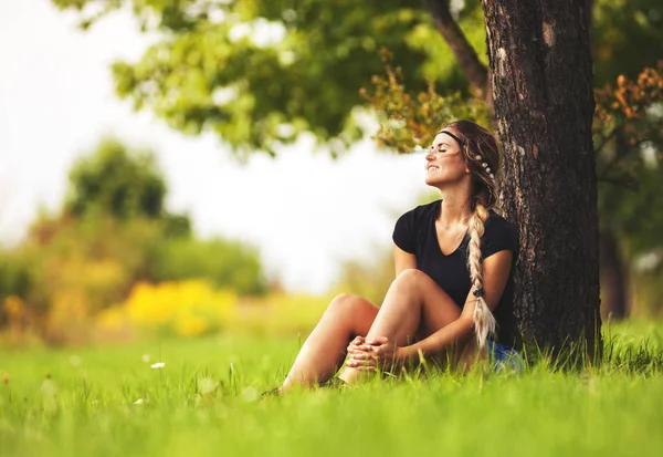 Hippie girl sitting under tree on meadow at summer day — Stock Photo, Image