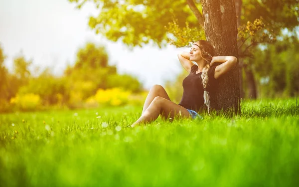 Hippie girl sitting under tree on meadow at summer day