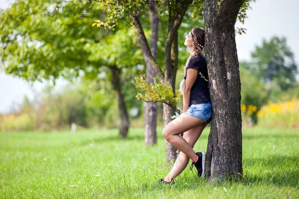 Ontspannen meisje permanent onder boom op weide op zomerdag — Stockfoto