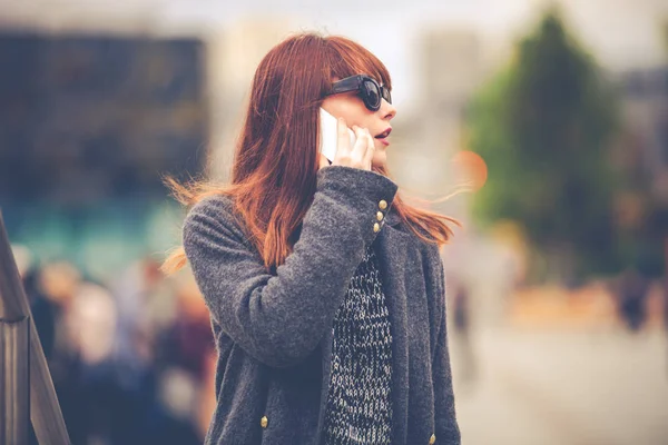 Mladá dívka v kabátě s mobilním telefonem na náměstí — Stock fotografie