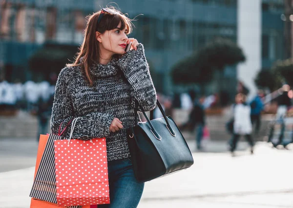 Mujer con bolsas de compras utilizando el teléfono móvil, escena de la ciudad — Foto de Stock