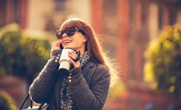 Mujer con taza de café hablando por teléfono móvil en la ciudad — Foto de Stock