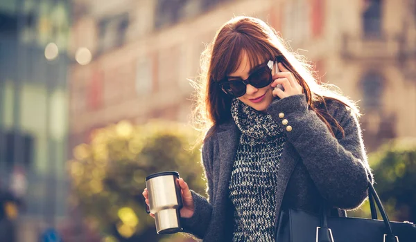 Жінка з чашкою кави говорить на мобільному телефоні в місті — стокове фото
