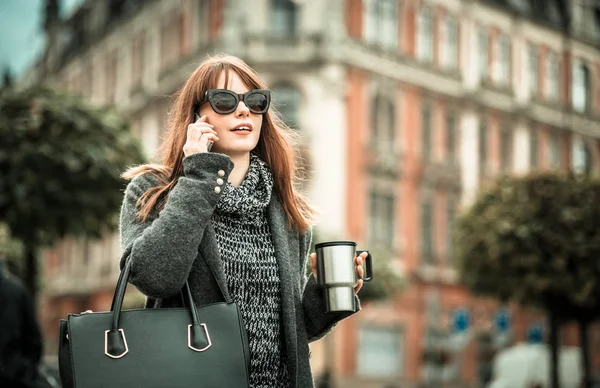 Городская сцена, женщина с чашкой кофе разговаривает по мобильному телефону в городе — стоковое фото