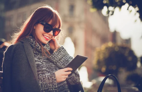 Mujer sonriente usando tableta o lector de libros electrónicos sentado en la ciudad, escena urbana —  Fotos de Stock