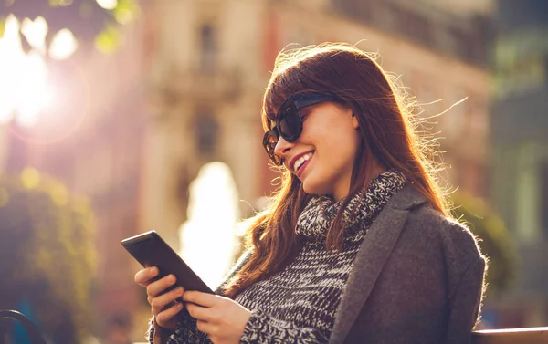 Улыбающаяся женщина, использующая планшет или электронную книгу, сидя на городской сцене — стоковое фото