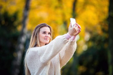 Tarafından cep telefonu sonbahar Park'ta yürüyordunuz sıcak kazak alarak resimdeki kadını