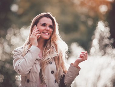 Şehirde yürüyüş ve Smartphone'da söz ceket giyen kadın gülümseyerek