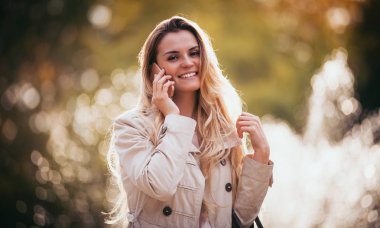 Şehirde yürüyüş ve Smartphone'da söz ceket giyen kadın gülümseyerek