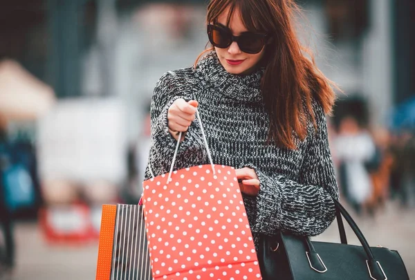 Mujer bonita en la calle de la ciudad mirando en la bolsa de compras — Foto de Stock