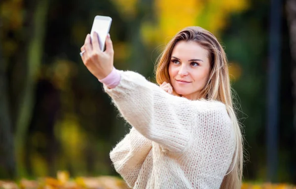 가 공원에서 산책 하는 휴대 전화로 따뜻한 스웨터 복용 사진에 여자 — 스톡 사진