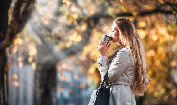 Mulher bonita bebendo café quente andando na rua de outono no dia ensolarado — Fotografia de Stock