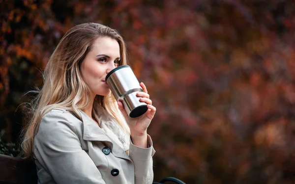 Beautiful woman drinking hot coffee from thermos cup — Stock Photo, Image