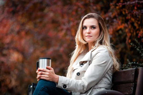 Beautiful woman sitting on bench with coffee thermos cup — Stock Photo, Image