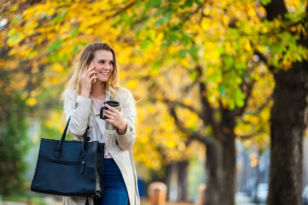 Красива жінка говорить смартфон, що йде барвистою осінньою вулицею — стокове фото