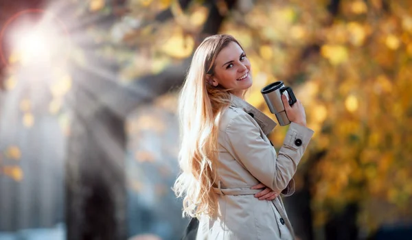 Schöne Frau mit heißem Kaffee, die an sonnigen Tagen auf der Herbststraße spaziert — Stockfoto