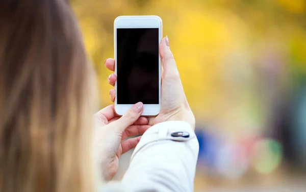 Closeup smartphone in hand with autumn street background — Stock Photo, Image