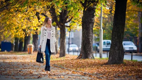 Smiling woman in coat walking on beautiful autumn street