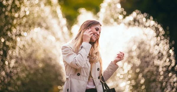 Mujer sonriente usando chaqueta caminando en la ciudad y hablando en el teléfono inteligente —  Fotos de Stock