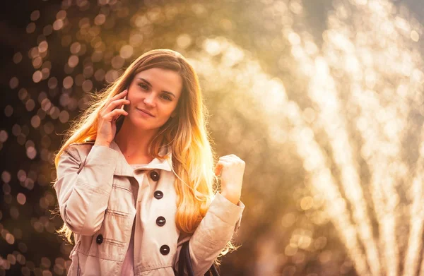 Lächelnde Frau im Mantel spaziert durch die Stadt und nutzt Smartphone — Stockfoto