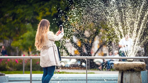 Kobieta w jesień miasta biorąc zdjęcie fontanny na smartphone — Zdjęcie stockowe