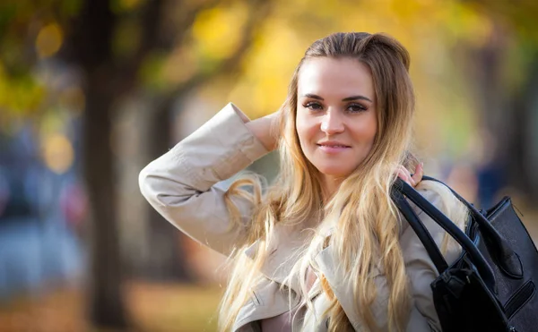 Mladá žena v plášti s úsměvem v barevné podzimní city — Stock fotografie