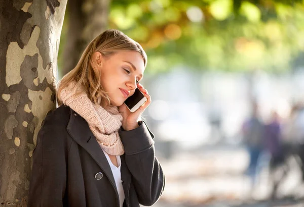 Женщина разговаривает по телефону на городской улице осенью — стоковое фото